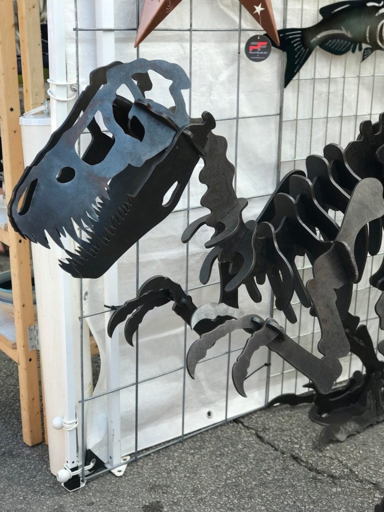 A black large metal dinosaur sculpture stands several feet tall