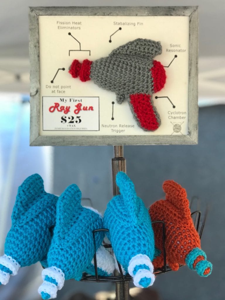 Crocheted ray gun display shows one ray gun with display arrows highlighting features and several more ray guns beneath