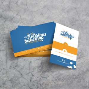 A stack of blue, white, and yellow business cards with a dynamic design for "the curious bakeshop"