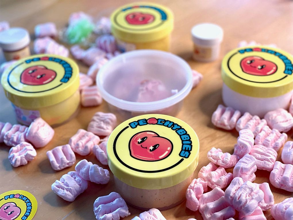 Cute smiling peach hearts on top of peachybbies slime containers surrounded by packing peanuts