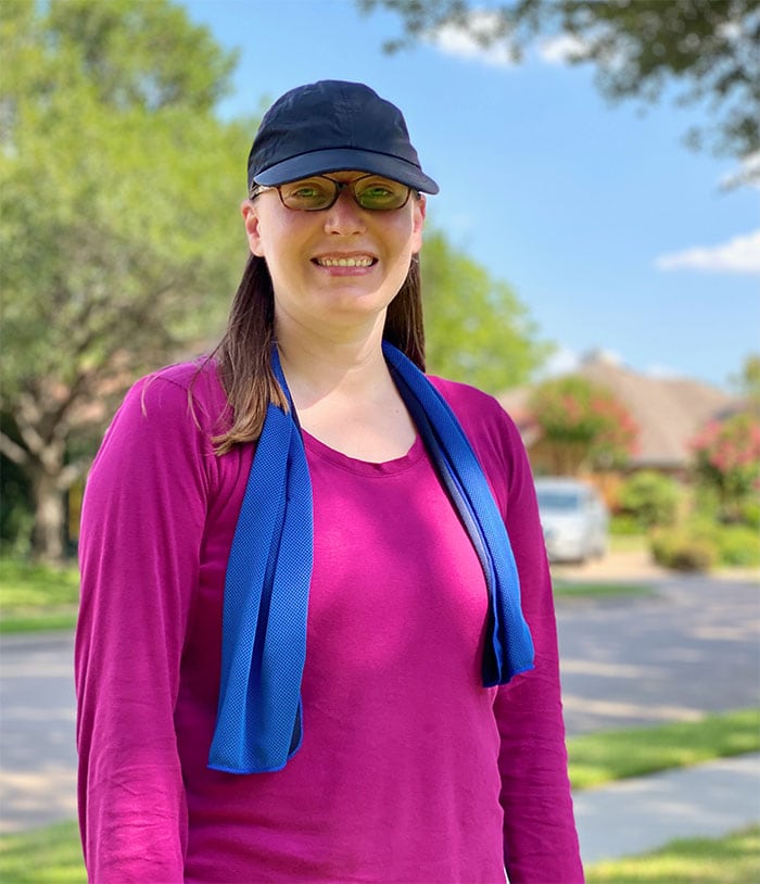 a woman in a purple shirt with a black hat wears a blue cooling towel around her neck