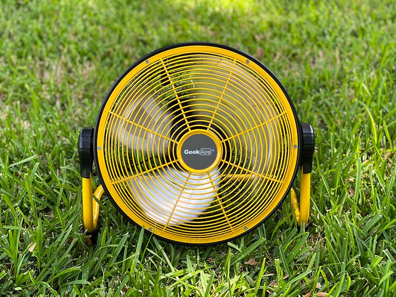 a yellow and black battery operated floor fan sits on the grass outside