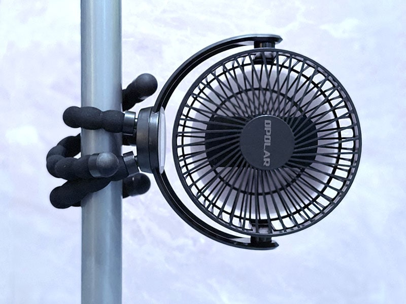 octopus tripod clip fan is wrapped around the leg of a canopy against a lilac background