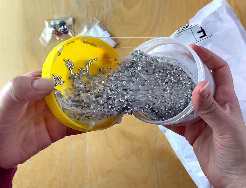 half open jar of sparkly crunchy slime spread between a clear container and a yellow lid being opened