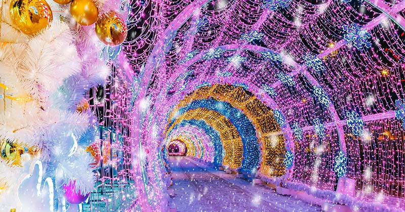 A road surrounded by a tunnel of lights, decorations, and ornaments.