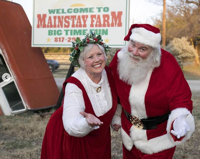 Mrs and Mr Santa Claus stand in front of a Mainstay Farm sign in their red velvet attire