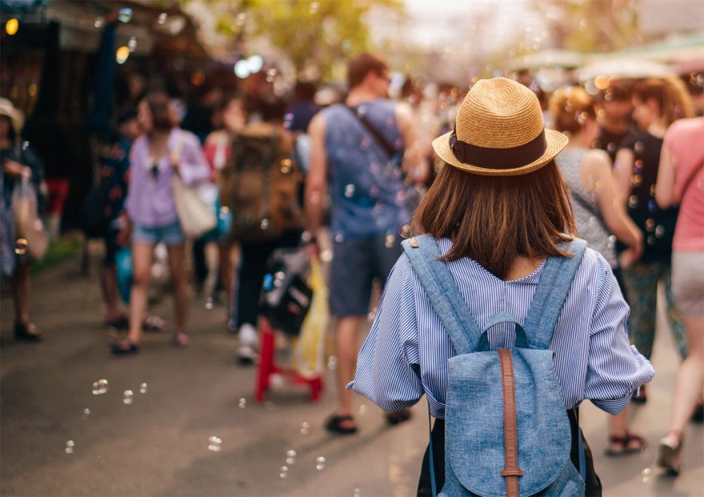 A girl with a hat and backup walks toward an outdoor event with bubbles in the air