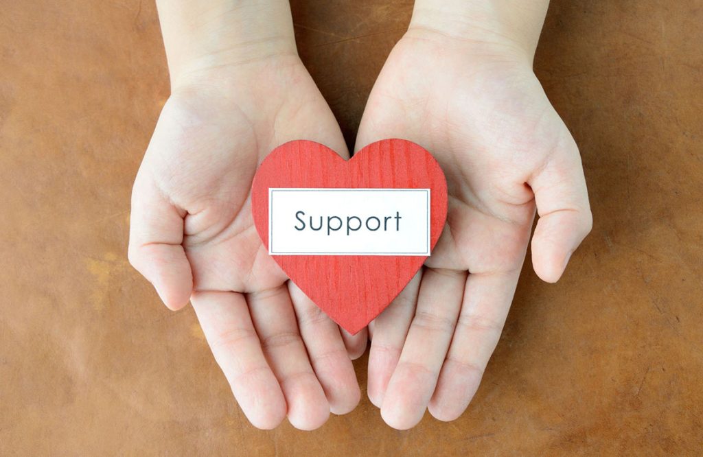 Open hands hold a red heart with the word "support"