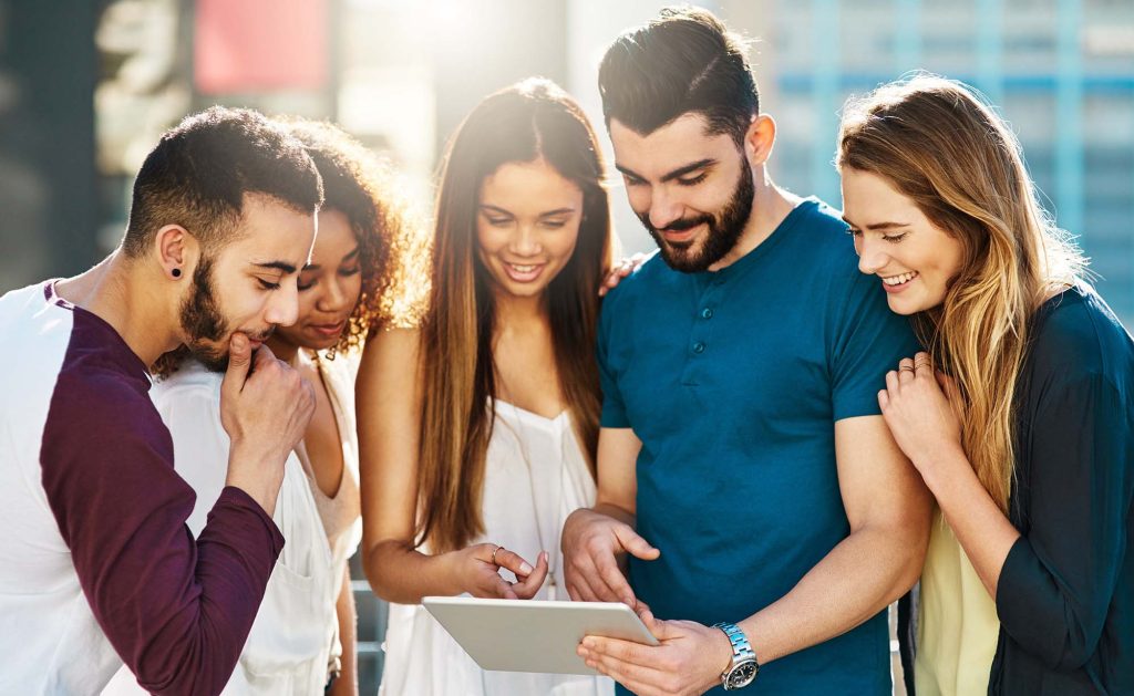 A group of people politely gathered around an ipad. Everyone is smiling.
