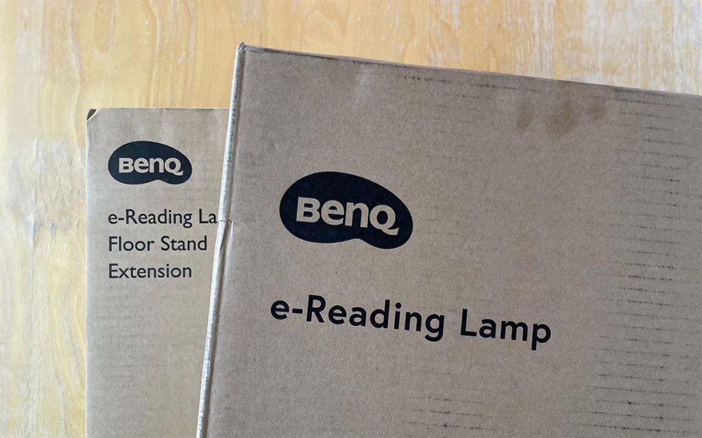 Two cardboard boxes sit on a table, the text "BenQ e-Reading Lamp" is visible