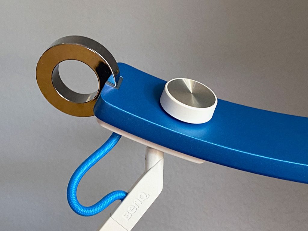 A blue lamp head is pictured close up with attention on the touch control loop (reflective silver) and control dial (white).